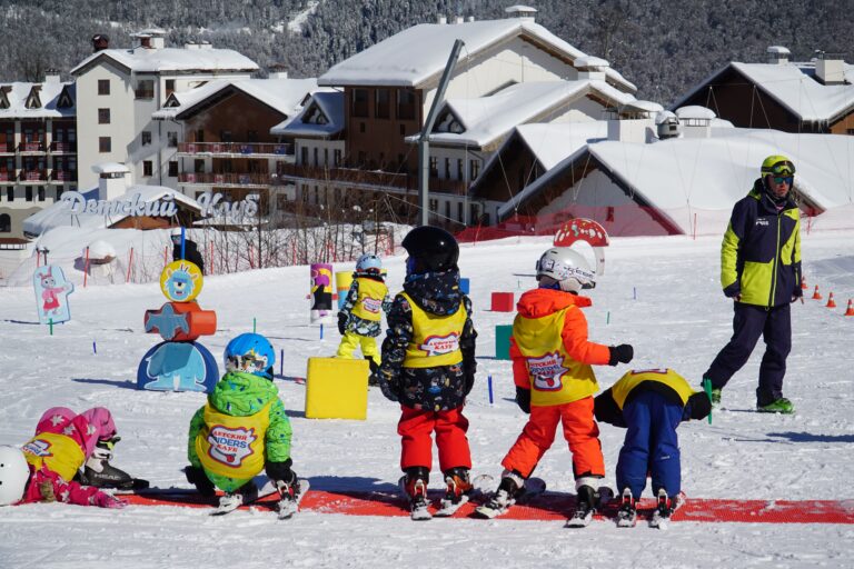 Kids in colorful outfits enjoying ski lessons on a snowy slope in Adlerskiy, Russia.